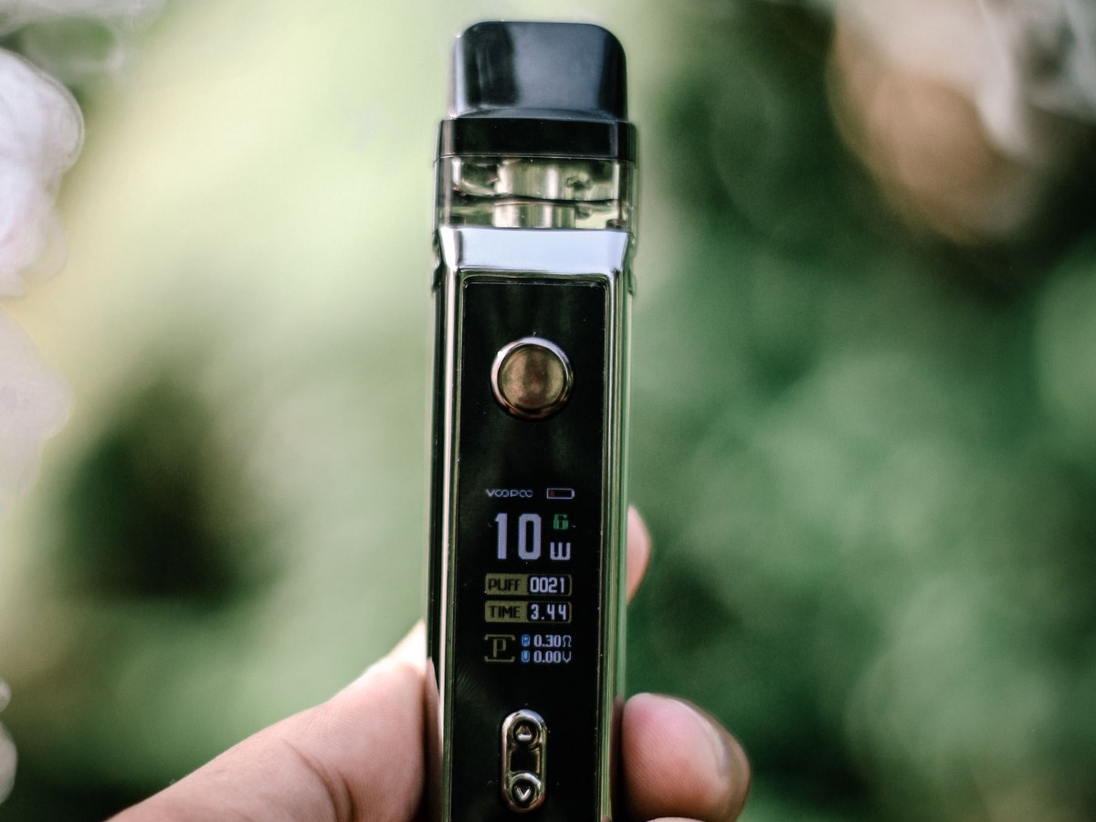 A hand holding a vape device with a small display